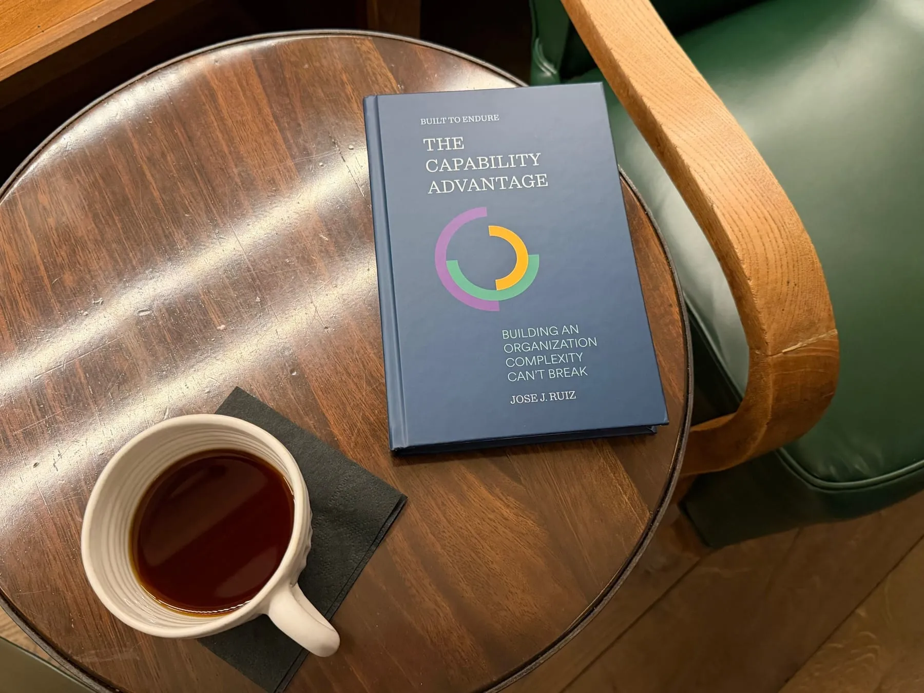 Hardcover copy of The Capability Advantage by Jose J. Ruiz resting on a wooden café table beside a cup of coffee.